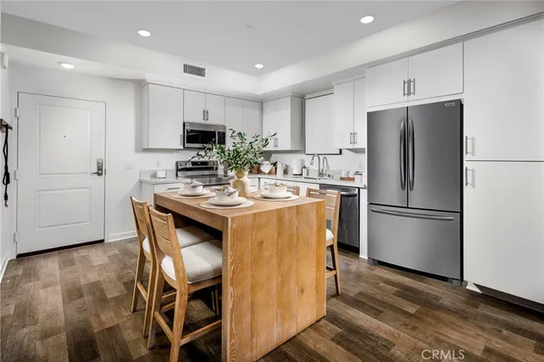 a kitchen with a refrigerator a microwave oven a sink and a dining table with wooden floor