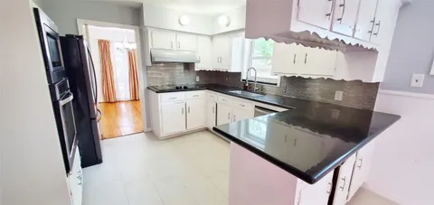 a kitchen with stainless steel appliances granite countertop a refrigerator a sink dishwasher a stove and white cabinets with wooden floor