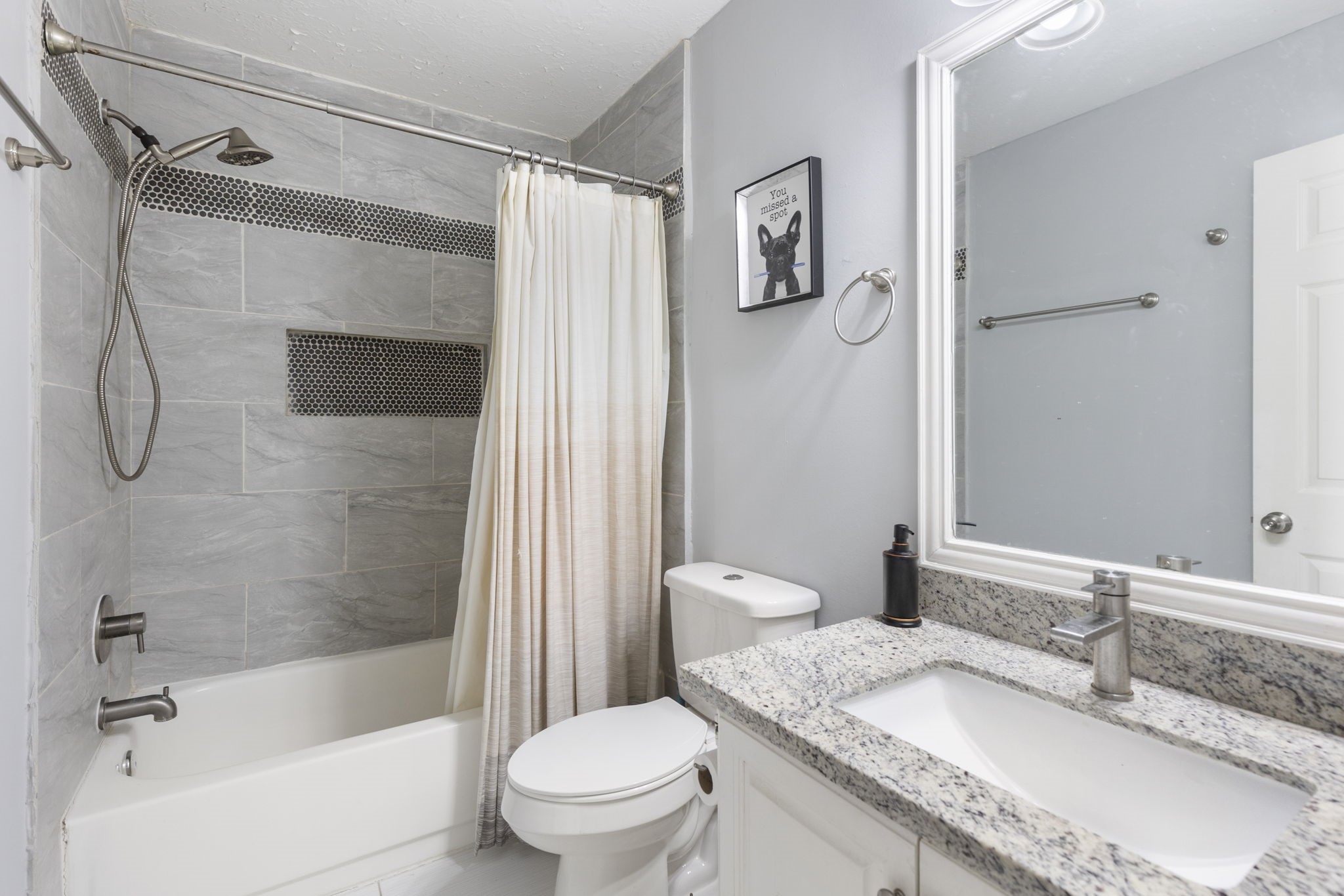 2110 Paso Rello Drive Houston, TX 77077 - Photo 34 of 41 This bathroom features a modern design with gray tile walls and a granite countertop. It includes a bathtub with a shower, a sleek faucet, and a stylish framed mirror. The decor is minimalist with a touch of elegance.