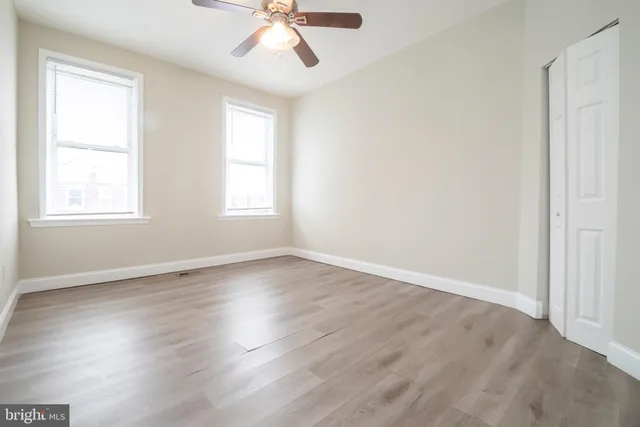 an empty room with wooden floor fan and windows