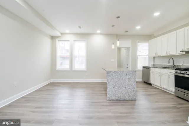 a living room with stainless steel appliances kitchen island granite countertop a stove a sink a refrigerator and white cabinets