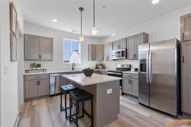 a kitchen with stainless steel appliances granite countertop a refrigerator a sink dishwasher a stove top oven a kitchen island and chairs with wooden floor