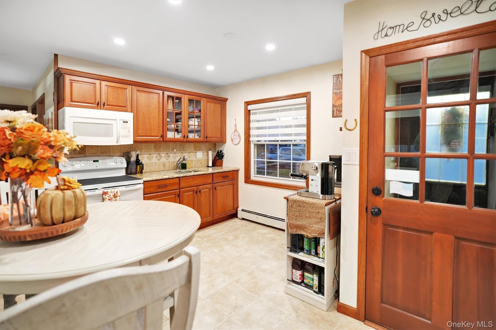 43 Ribbon Lane Wantagh, NY 11793 - Photo 6 of 36 Kitchen with brown cabinets, white appliances, glass insert cabinets, a baseboard radiator, and recessed lighting