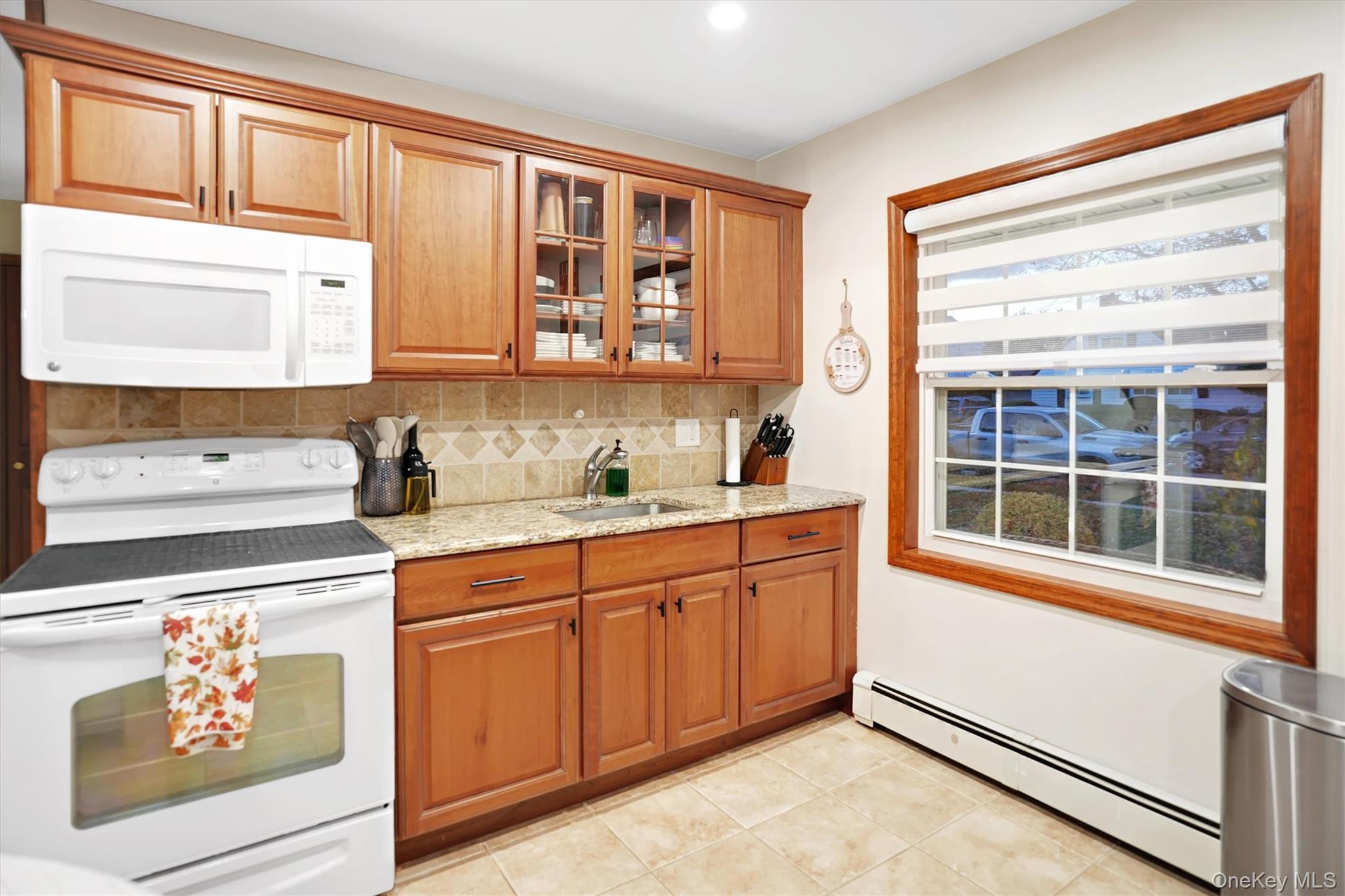 43 Ribbon Lane Wantagh, NY 11793 - Photo 10 of 36 Kitchen featuring white appliances, baseboard heating, light stone countertops, decorative backsplash, and glass insert cabinets