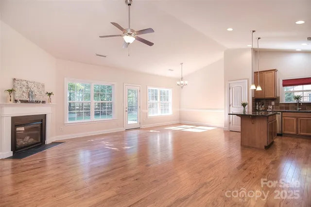 a view of an empty room with wooden floor and a kitchen