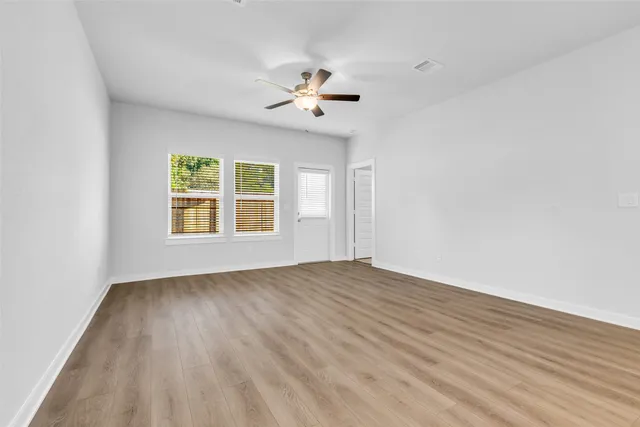 an empty room with wooden floor chandelier fan and windows