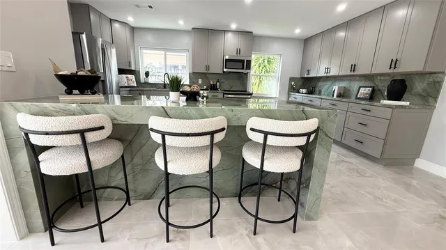 a kitchen with stainless steel appliances kitchen island granite countertop a table chairs and a refrigerator