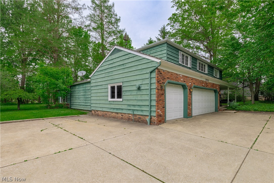 25001 Letchworth Road Beachwood, OH 44122 - Photo 44 of 50 Two-car garage with brick facade and green siding, featuring a concrete driveway and mature trees surrounding the property
