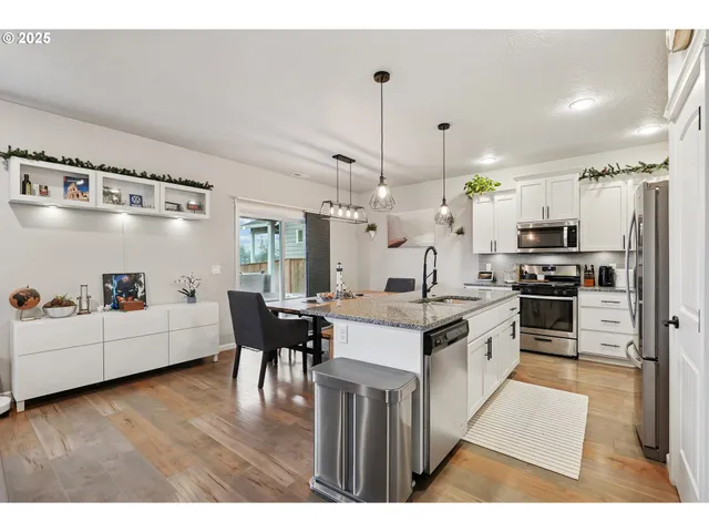 a kitchen with granite countertop a refrigerator a stove a sink dishwasher a dining table and chairs with wooden floor