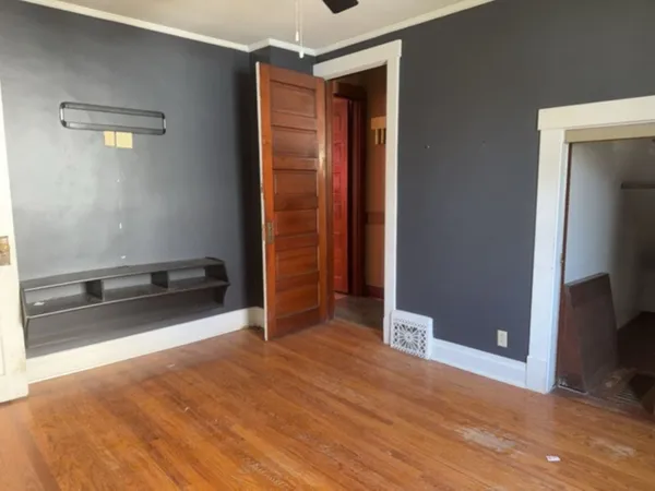 an empty room with wooden floor and way to kitchen