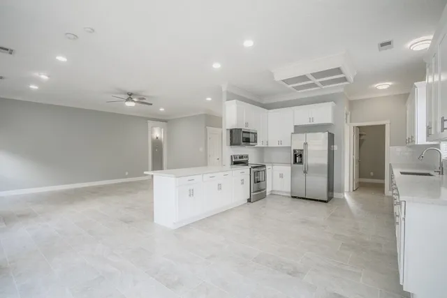 a large white kitchen with stainless steel appliances cabinets a sink and a refrigerator