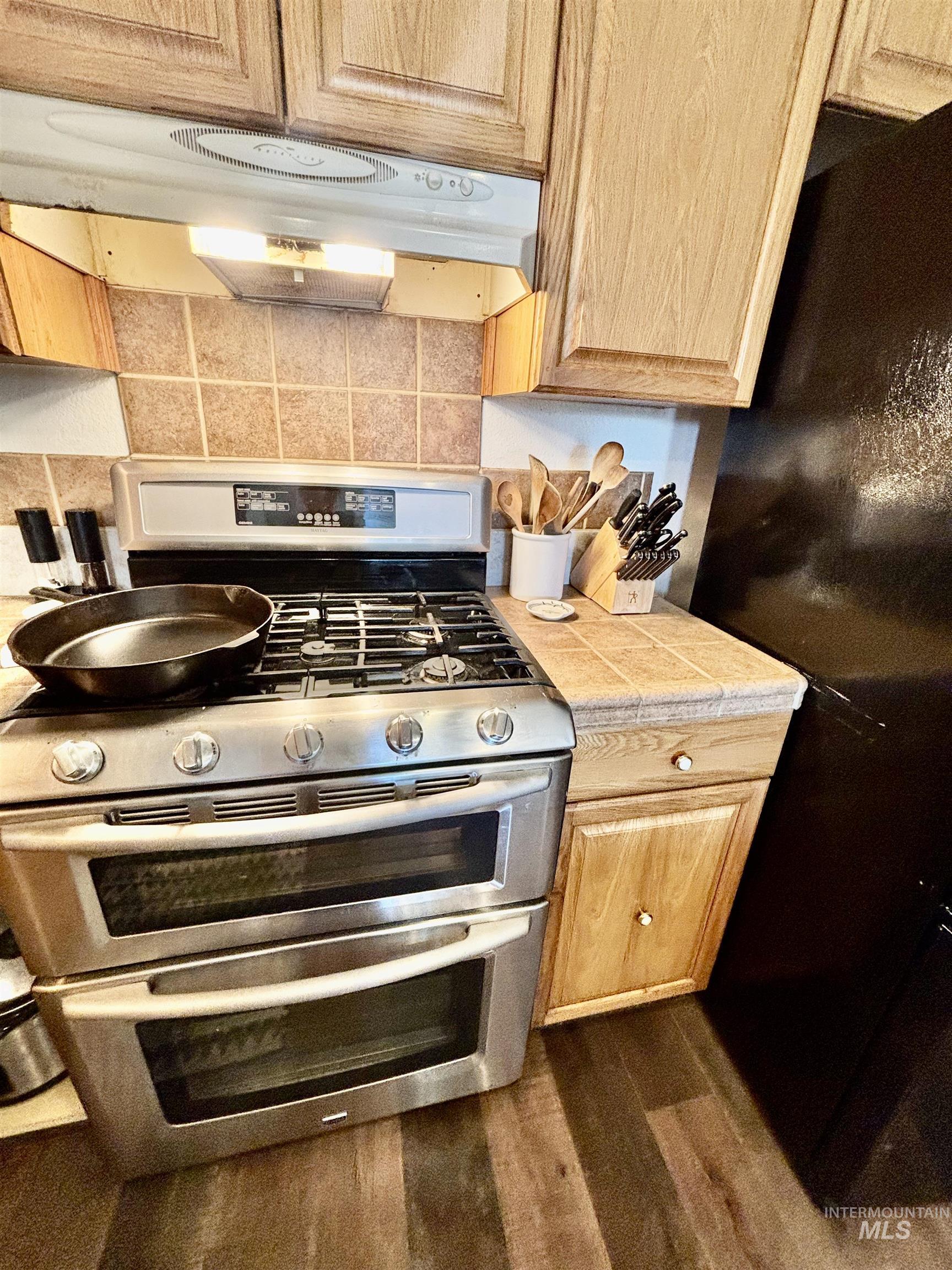 23626 Boise River Road Caldwell, ID 83607 - Photo 11 of 49 Stainless steel double oven range with gas cooktop, tile backsplash, wood-finish cabinetry, and wood-finish flooring