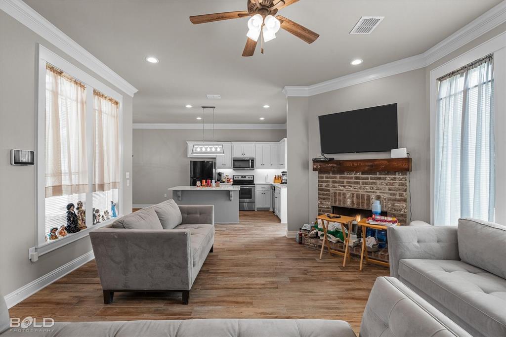 6896 Bethany Reed Circle Blanchard, LA 71107 - Photo 14 of 37 Open-concept living area with wood-finish flooring, a brick fireplace with a wood mantle, and crown molding