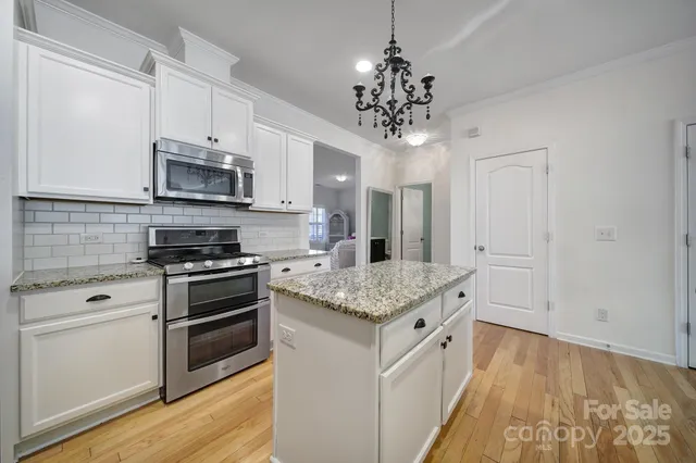 a kitchen with stainless steel appliances granite countertop a sink stove oven and white cabinets with wooden floor
