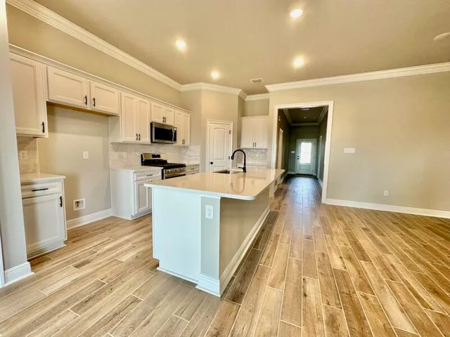 a kitchen with stainless steel appliances a stove top oven a sink a refrigerator white cabinets and wooden floor