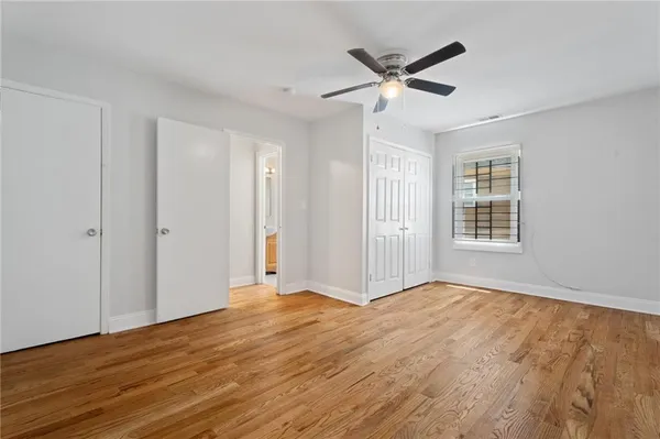 a view of an empty room with wooden floor and a ceiling fan