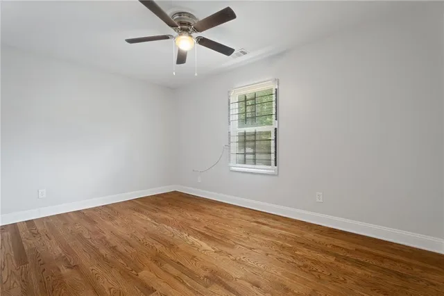 an empty room with wooden floor ceiling fan and windows