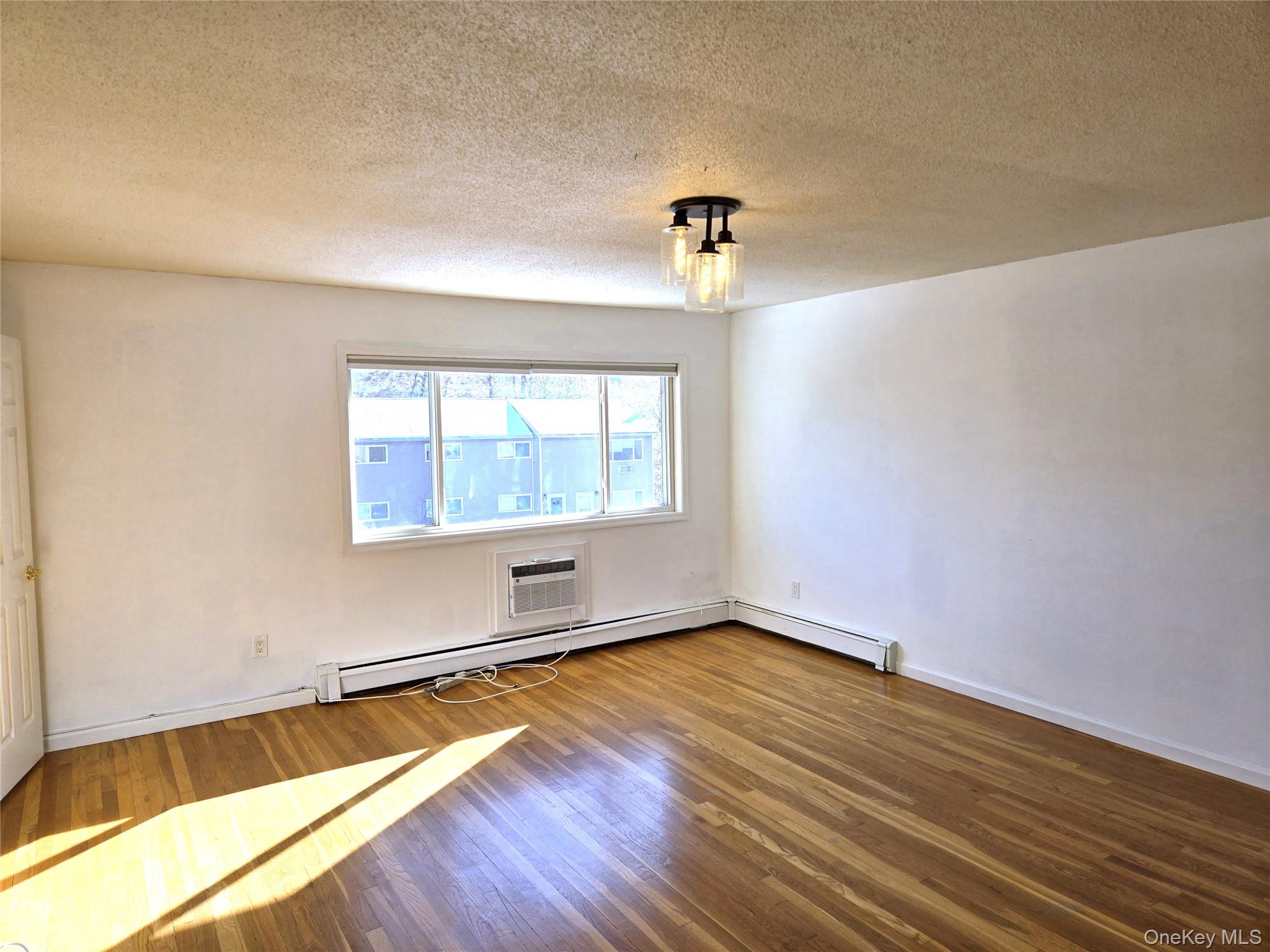9 Fishkill Glen Drive, Unit F Fishkill, NY 12524 - Photo 3 of 10 Unfurnished room with hardwood / wood-style flooring, a textured ceiling, a baseboard heating unit, a wall unit AC, and a baseboard radiator