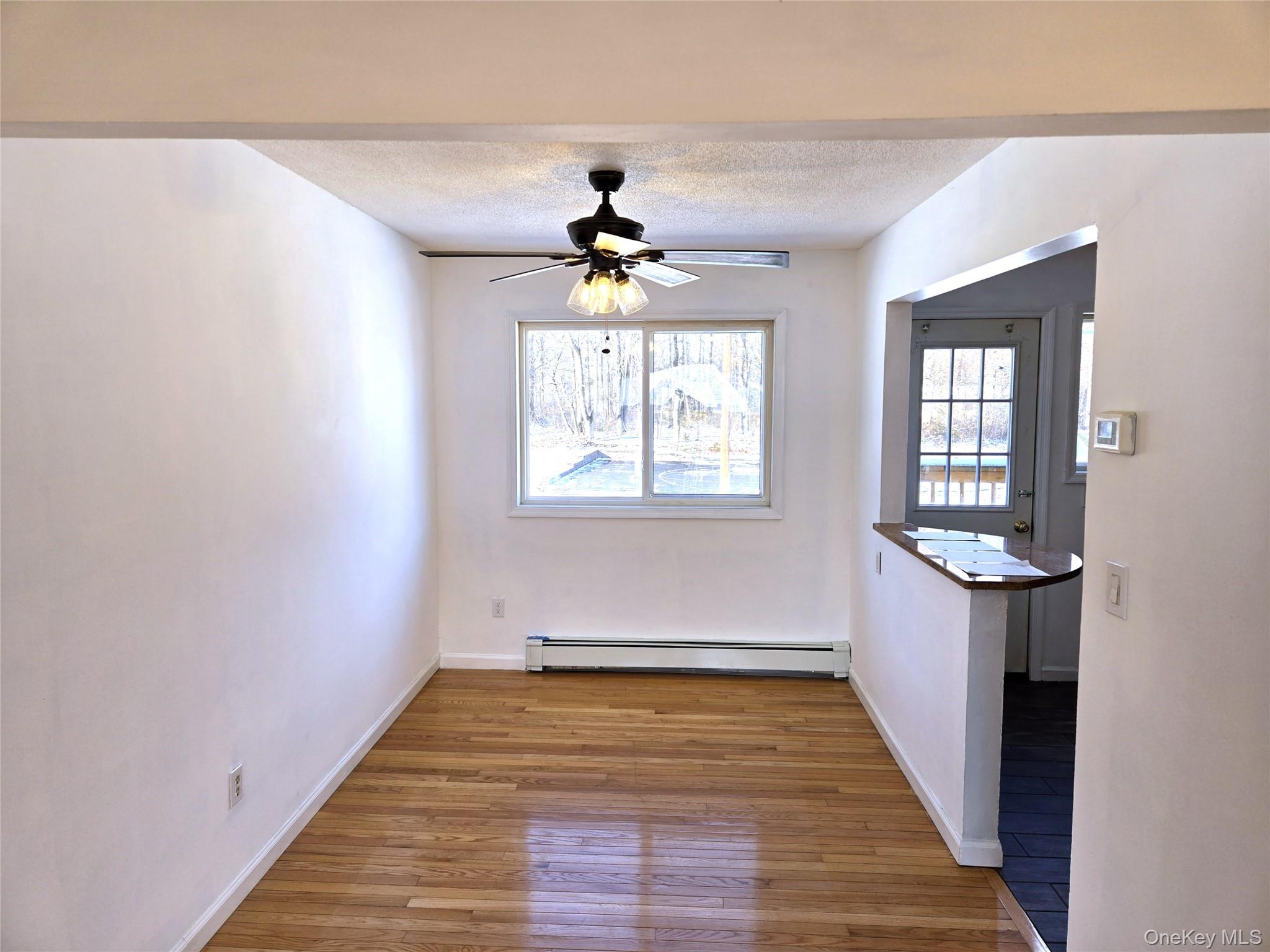9 Fishkill Glen Drive, Unit F Fishkill, NY 12524 - Photo 4 of 10 Unfurnished dining area featuring wood-type flooring, a baseboard heating unit, a textured ceiling, and a ceiling fan