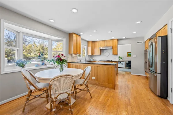 a kitchen with stainless steel appliances granite countertop a refrigerator a stove top oven and a dining table with wooden floor