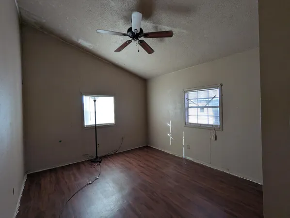 a view of empty room with wooden floor and fan
