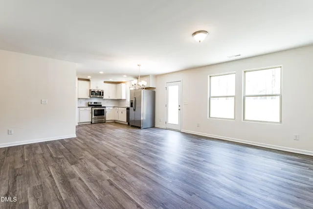 an empty room with wooden floor kitchen stove and windows
