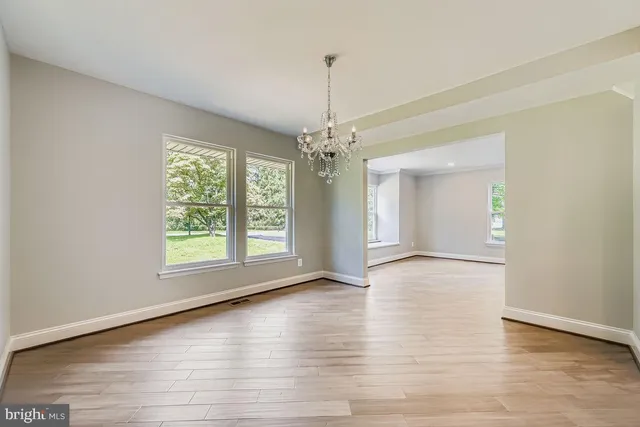 an empty room with wooden floor chandelier and windows