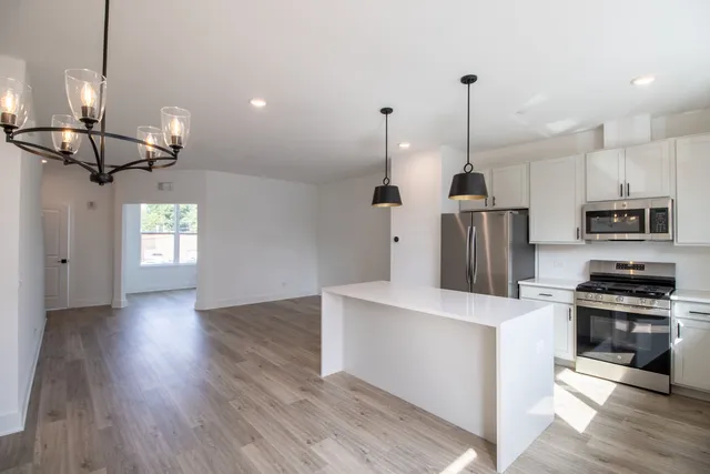 a kitchen with stainless steel appliances kitchen island a refrigerator and a wooden floor
