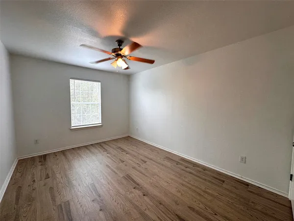 an empty room with wooden floor chandelier fan and windows
