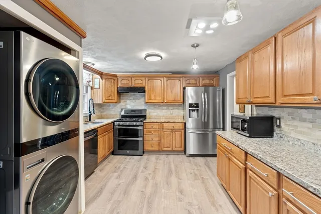 a kitchen with stainless steel appliances granite countertop a sink a stove a refrigerator cabinets and a window
