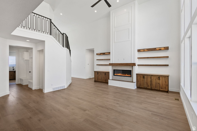 692 East Mountain Road North Ogden, UT 84414 - Photo 5 of 17 Great room featuring a tall vaulted ceiling, wood-finish flooring, a contemporary fireplace with a wood mantle, custom built-in cabinetry, and a striking staircase with decorative metal railing