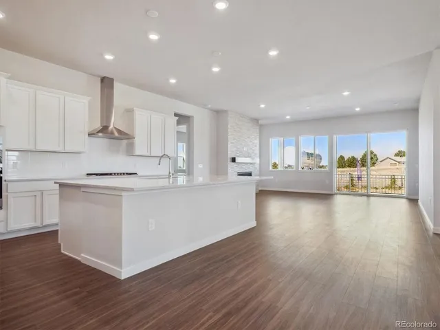 a large white kitchen with kitchen island a sink dishwasher a stove a refrigerator and white cabinets with wooden floor