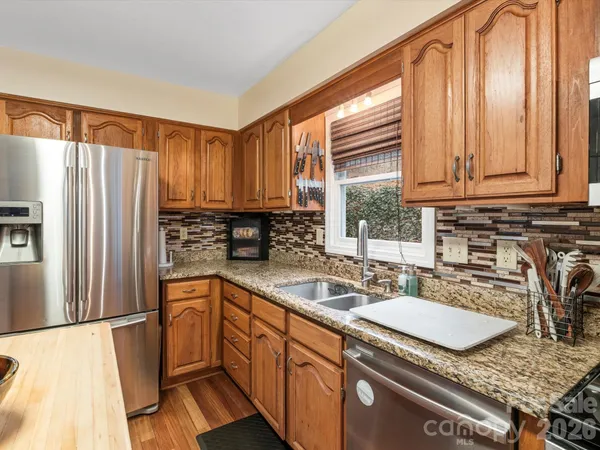 a kitchen with granite countertop a sink a counter top space cabinets stainless steel appliances and a window