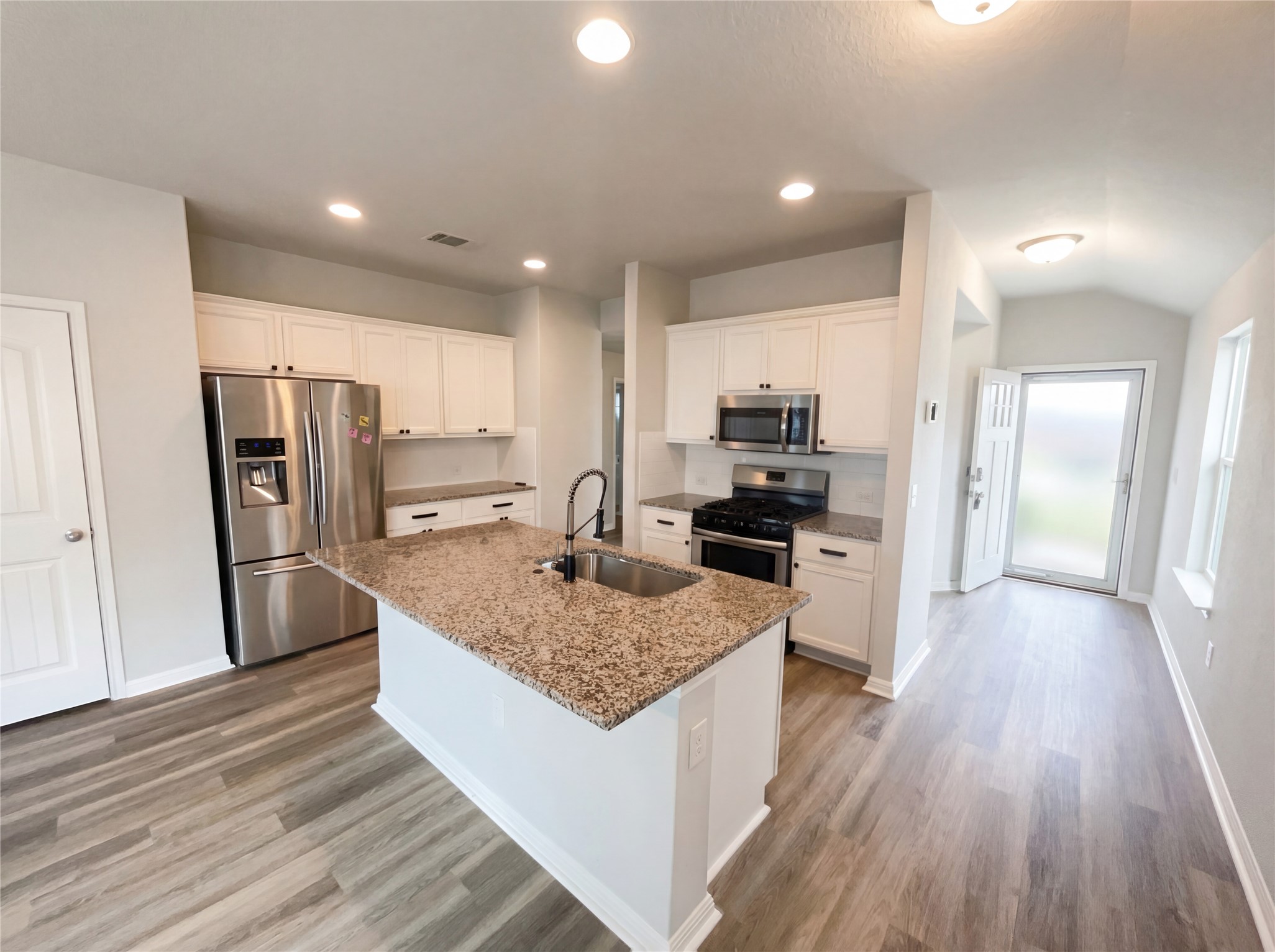 413 Dubina Avenue Georgetown, TX 78626 - Photo 7 of 22 Kitchen featuring stainless steel appliances, white cabinets, light stone counters, light wood-type flooring, and an island with sink