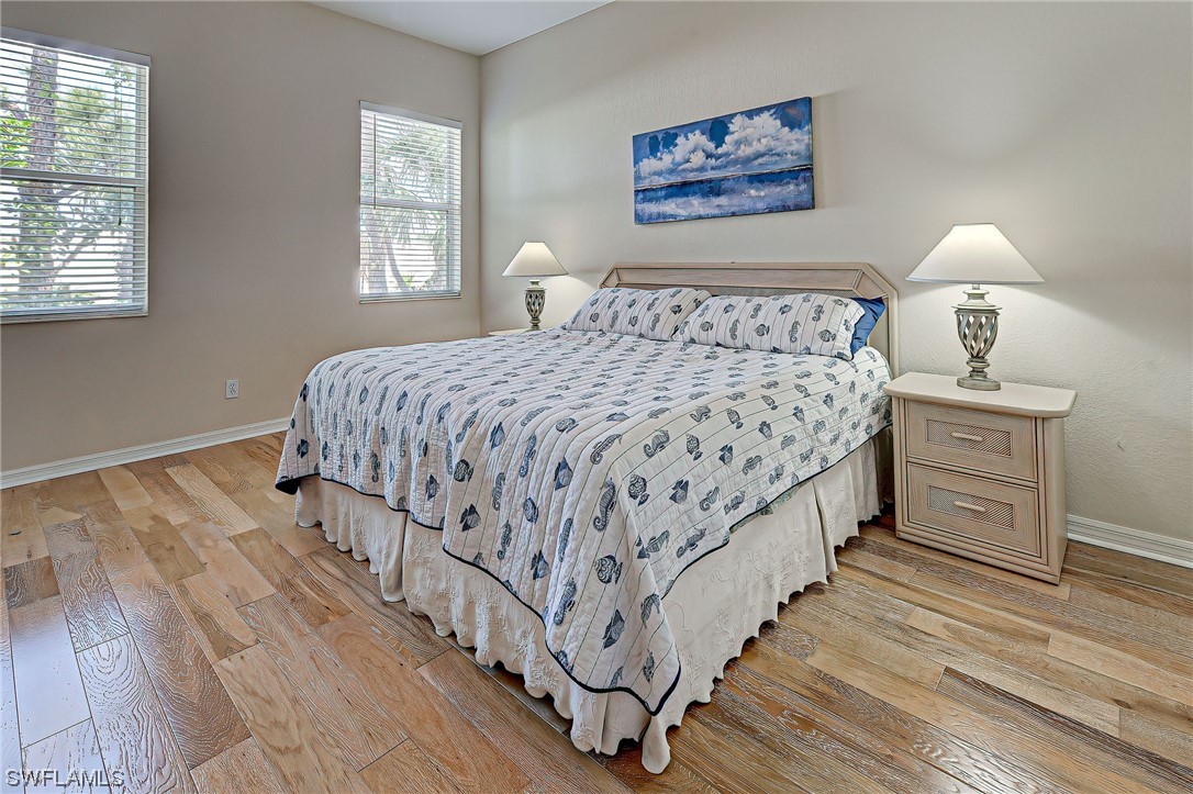 604 Ravinia Circle, Unit 604 Venice, FL 34292 - Photo 26 of 37 a bedroom with a bed and a lamp on dresser with wooden floor