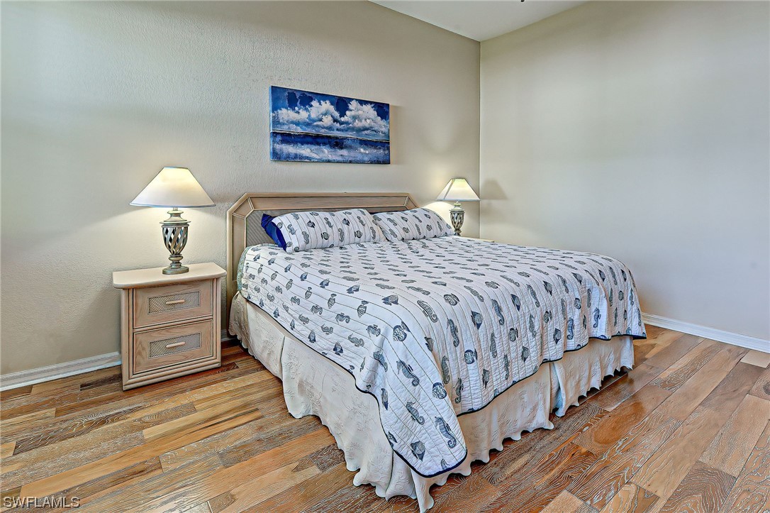 604 Ravinia Circle, Unit 604 Venice, FL 34292 - Photo 29 of 37 a bedroom with a bed and a lamp on dresser with wooden floor