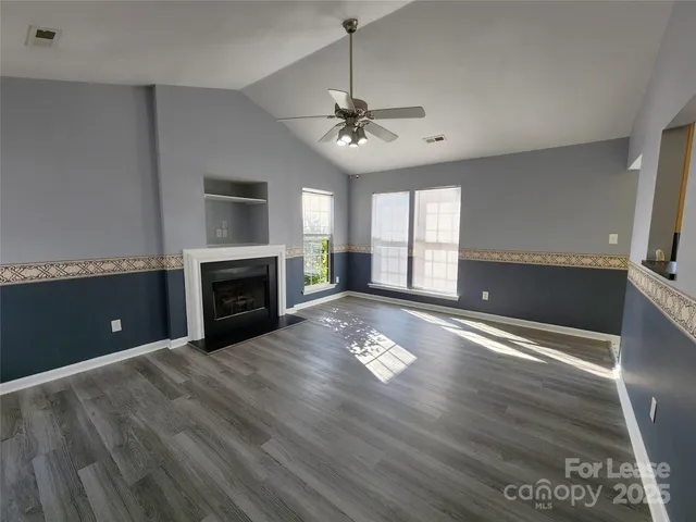 a view of a livingroom with a fireplace a ceiling fan and windows
