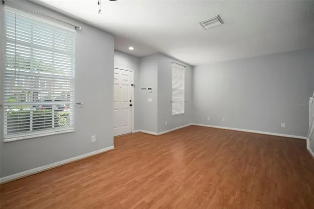 a view of an empty room with wooden floor and a ceiling fan