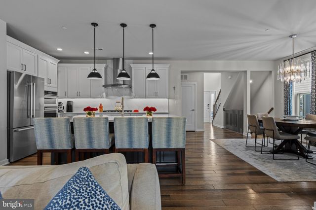 a kitchen with granite countertop a stove a sink a center island with living room furniture and a flat screen tv