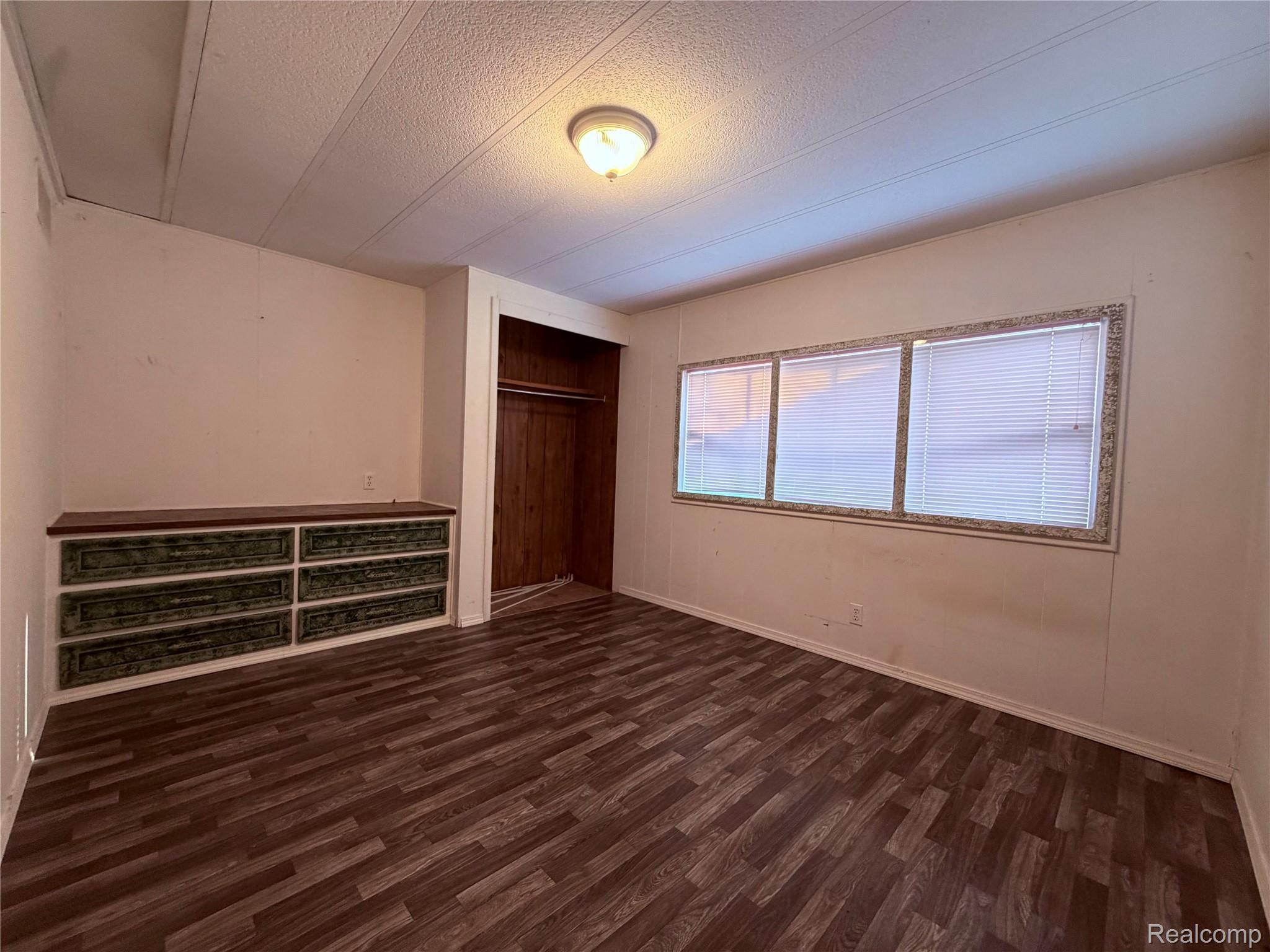 5656 Delong Road Deford, MI 48729 - Photo 14 of 22 Wood-finish flooring, built-in dresser with six drawers, wood-paneled closet, three windows with blinds, and a flush-mount ceiling light