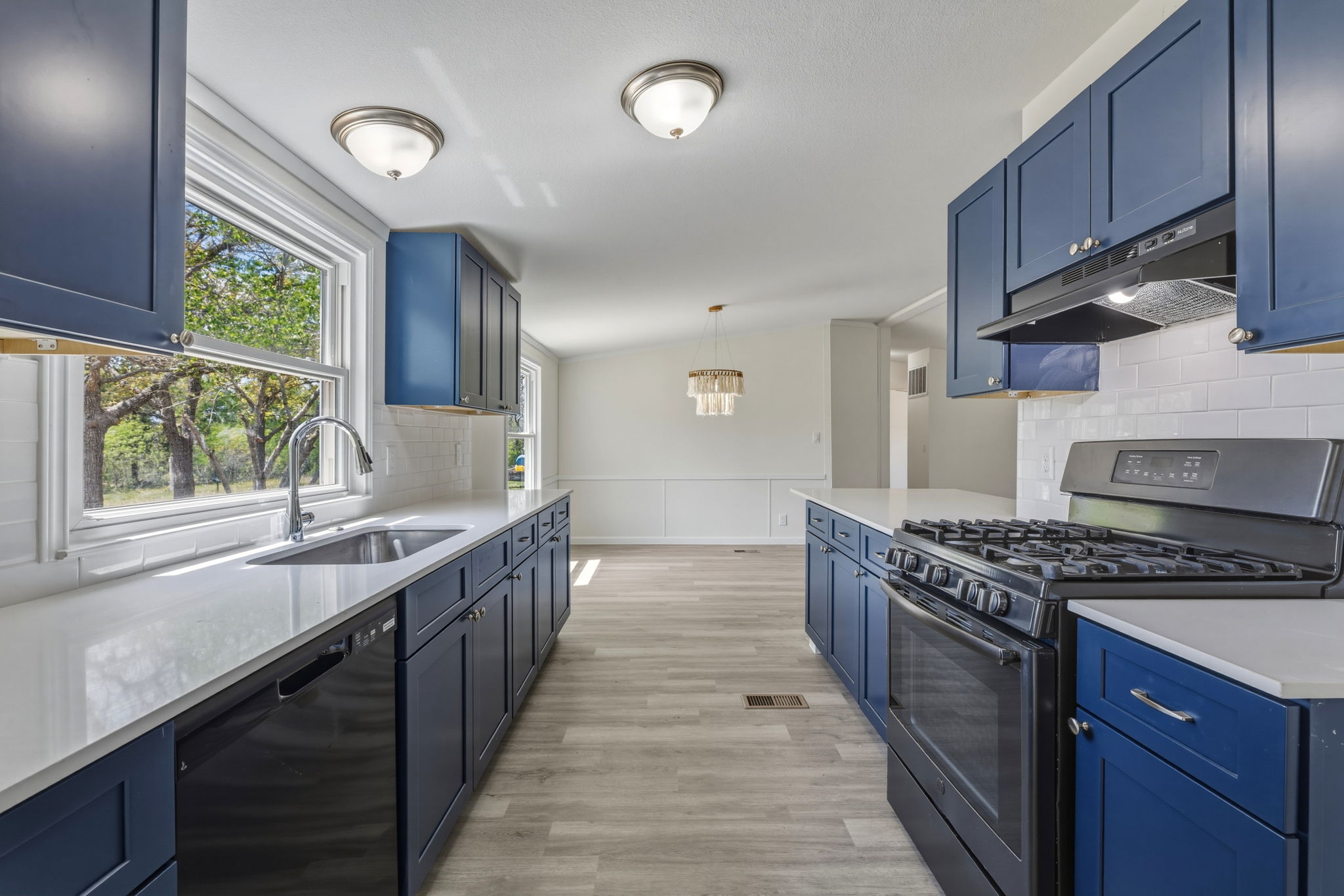 340 Red Hawk Drive Dale, TX 78616 - Photo 14 of 38 Kitchen featuring blue cabinets, backsplash, range and range hood, dishwasher, light colored floors, and quartz countertops,