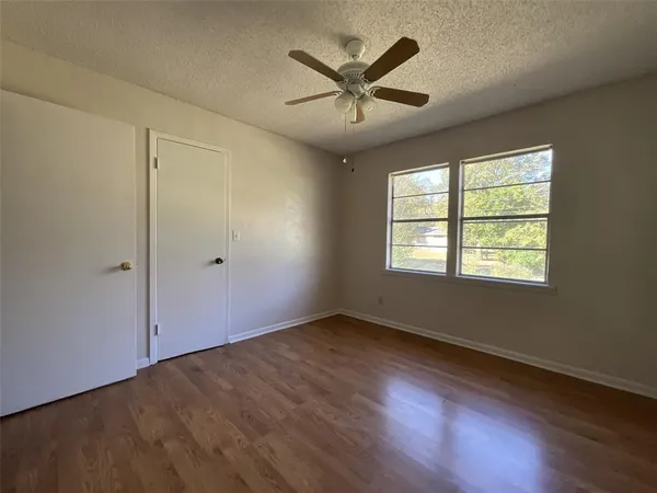 an empty room with wooden floor ceiling fan and windows