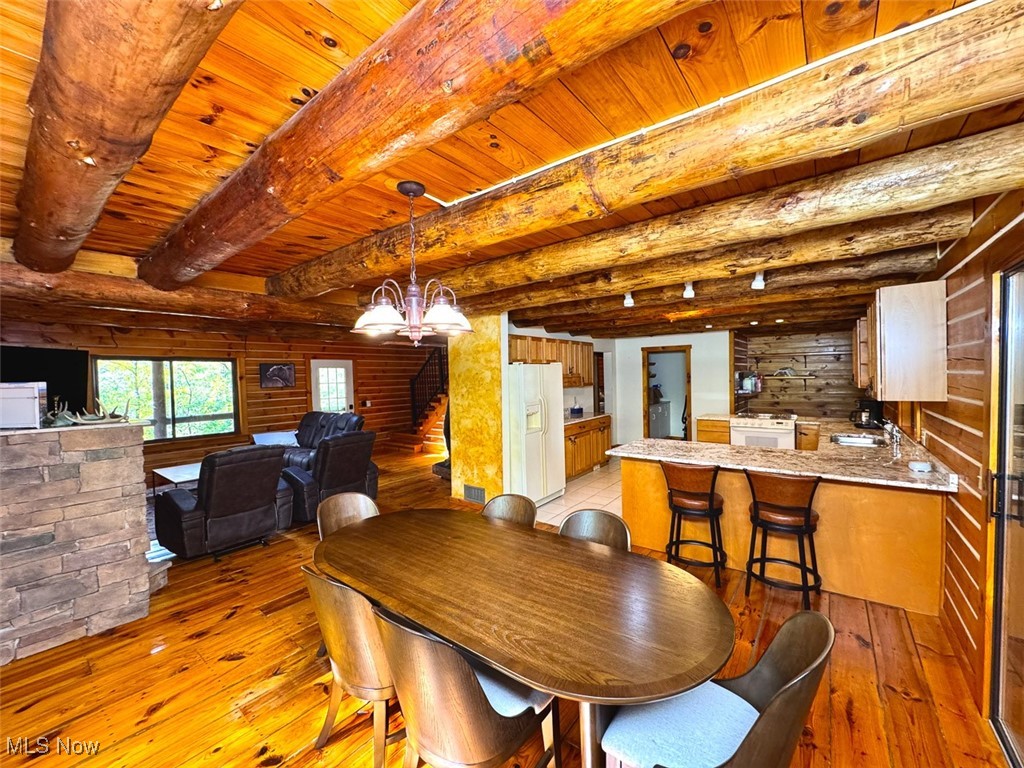 18063 Sligo Road Freeport, OH 43973 - Photo 36 of 50 Dining space featuring a wooden ceiling with exposed beams, light wood-style flooring, a chandelier, wooden walls, and stairway