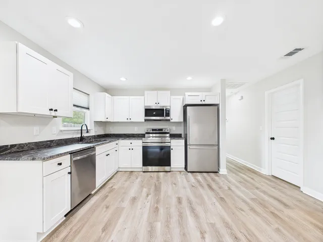 a kitchen with granite countertop a refrigerator oven a sink dishwasher and white cabinets with wooden floor