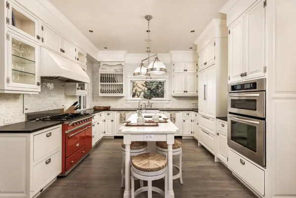 a large white kitchen with stainless steel appliances granite countertop a stove a sink dishwasher a dining table and chairs with wooden floor