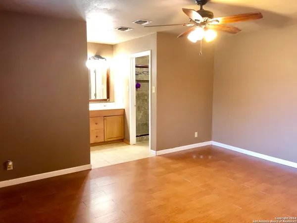 an empty room with wooden floor fan and windows