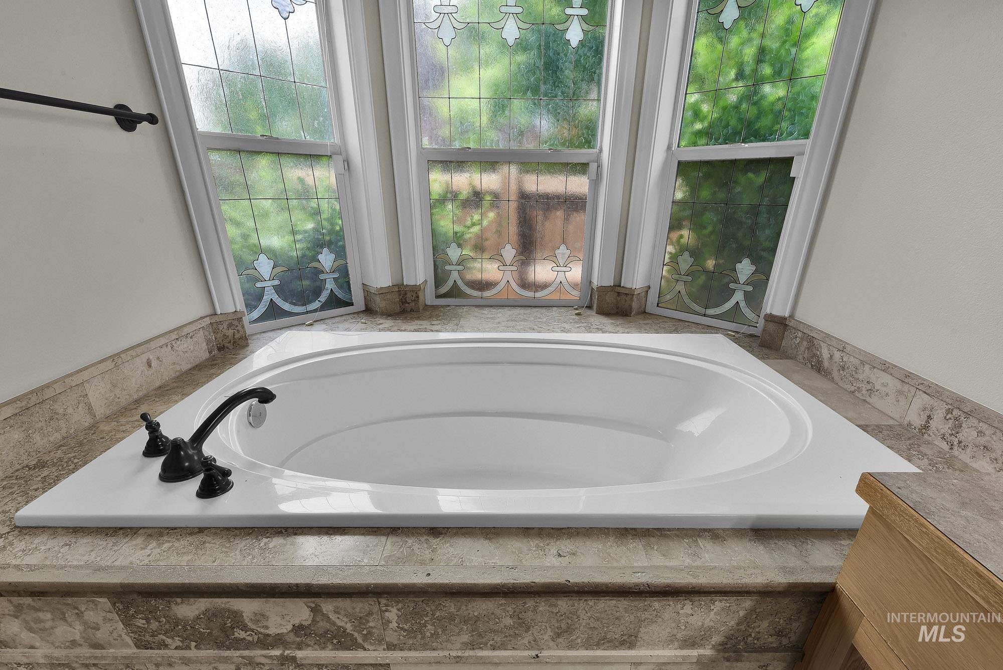 2172 West Cedar Grove Street Meridian, ID 83646 - Photo 16 of 49 Built-in garden tub with dark bronze fixtures, surrounded by stone tile and a white solid-surface deck
