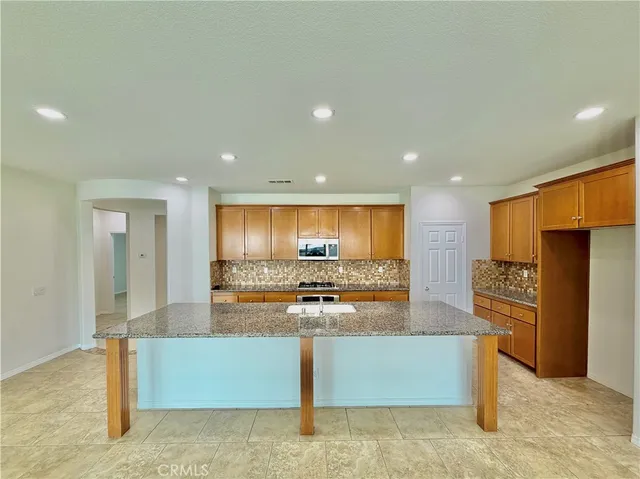 a large kitchen with stainless steel appliances kitchen island granite countertop a refrigerator and a stove