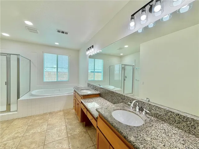 a spacious bathroom with a granite countertop double vanity sink a mirror and a bathtub