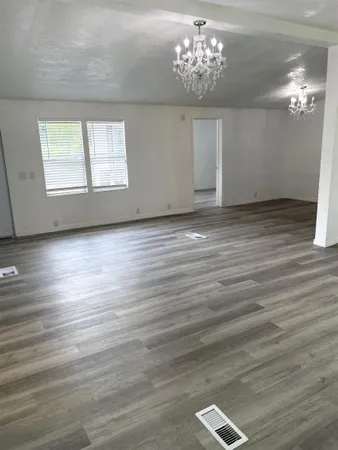 an empty room with wooden floor chandelier and windows